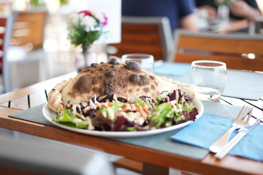 Un calzone doré sorti du four à bois, servi avec une salade
